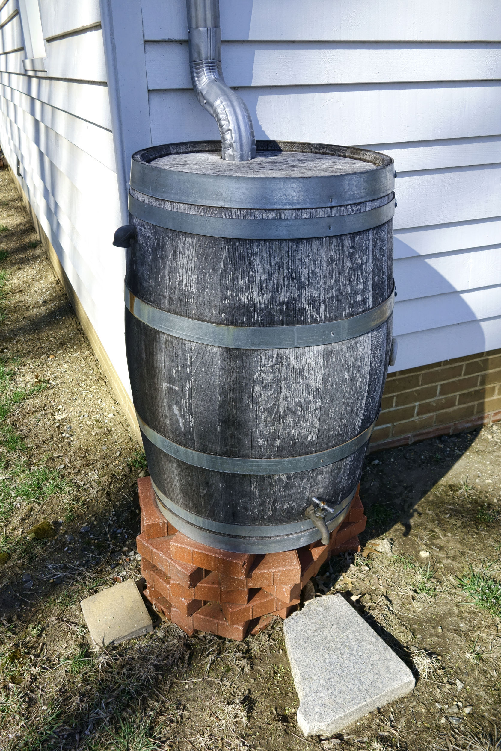 wood rainwater tank rain barrel for storm water runoff collection and recycling reuse with irrigation spigot at the corner of a rural house building